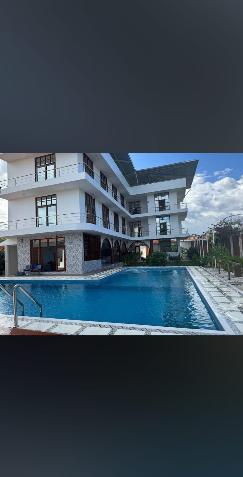 Modern white residential building with swimming pool, lounge chairs, and mountain backdrop under blue sky