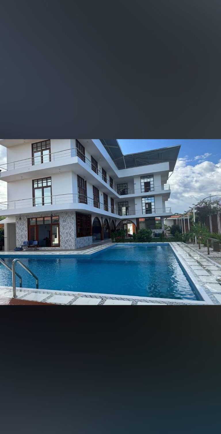 Modern white residential building with swimming pool, lounge chairs, and mountain backdrop under blue sky