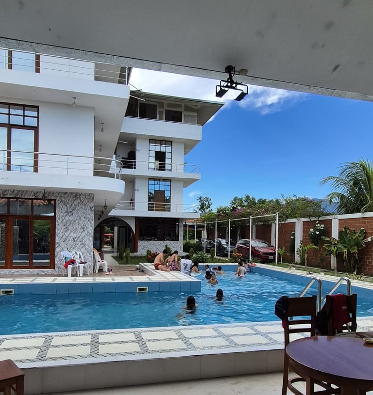 Modern white residential building with swimming pool, lounge chairs, and guests swimming on a sunny day with blue sky