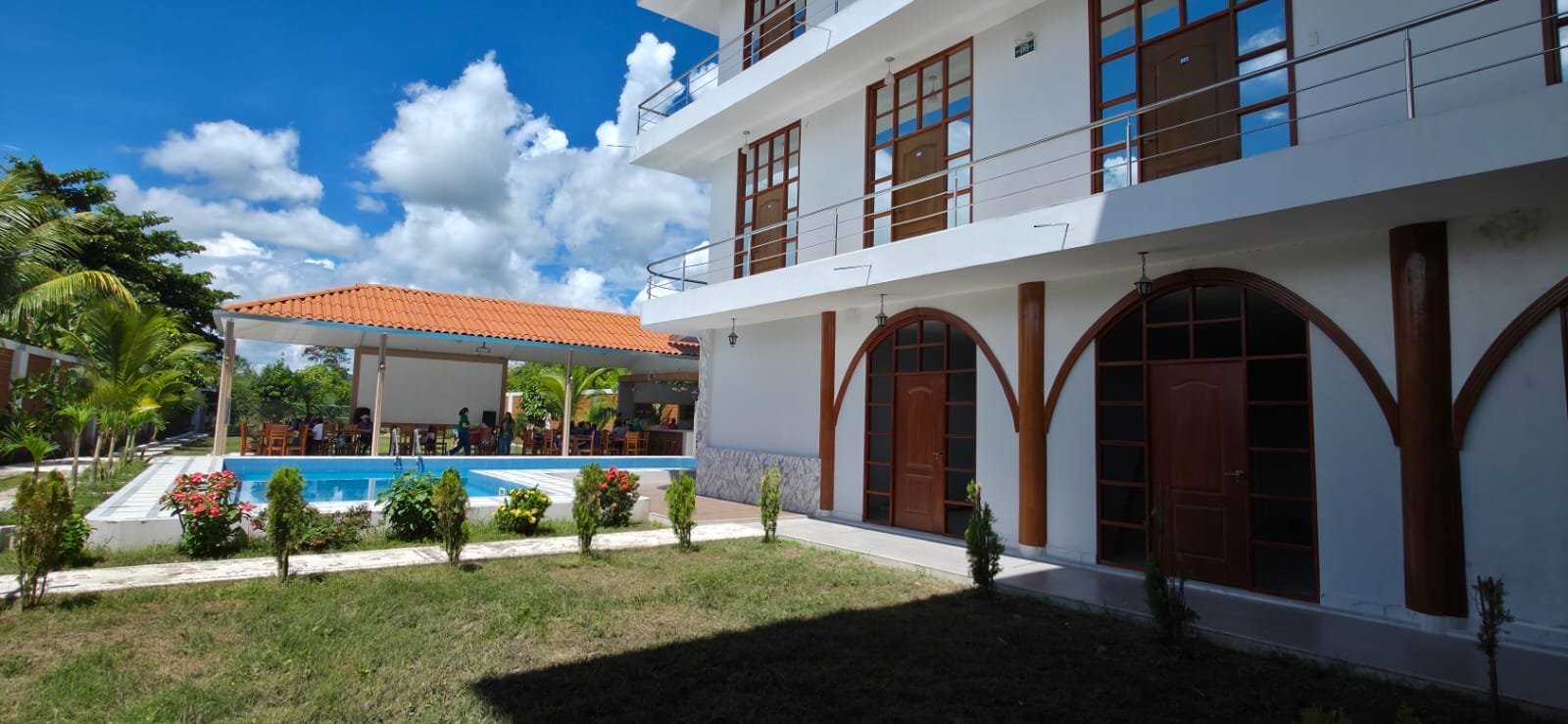 Modern white house with arched entryways, pool in background, manicured lawn, and blue sky with clouds