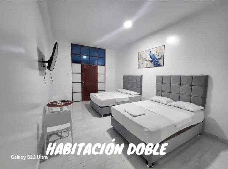 Modern hotel room with two queen beds with gray headboards, white bedding, minimalist furniture, and contemporary ceiling lights