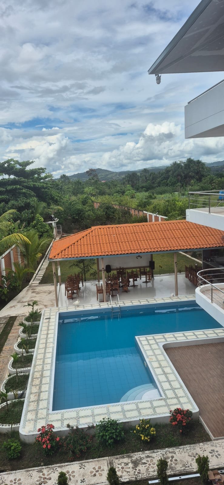 Modern tropical home with blue swimming pool, terracotta roof, white deck, and lush green mountains in the background